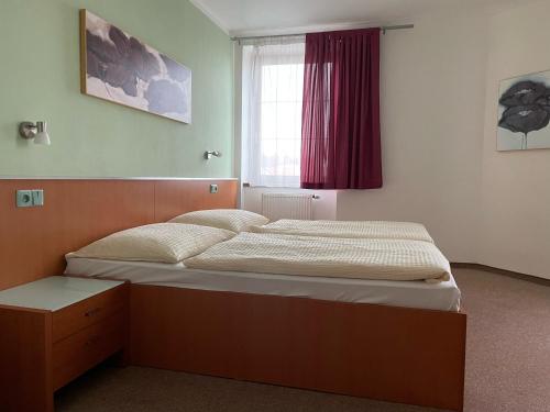 Bett in einem Zimmer mit rotem Fenster in der Unterkunft Hotel Ostrov Garni in Sadská