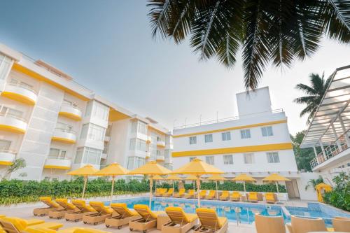 a hotel with chairs and umbrellas and a swimming pool at BloomSuites l Calangute in Calangute