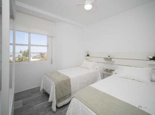 two beds in a white room with a window at Balcón a Doñana in Sanlúcar de Barrameda