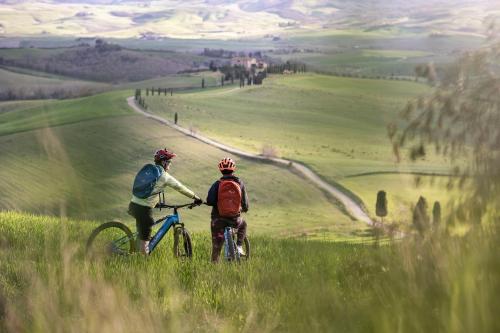 duas pessoas a andar de bicicleta numa colina relvada em Adler Spa Resort Thermae em Bagno Vignoni
