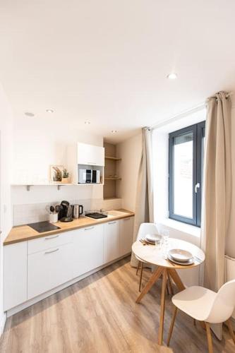 une cuisine avec des armoires blanches et une table et des chaises dans l'établissement Morphée - Résidence Hestia, à Saint-Étienne