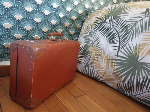 una valigia marrone seduta sul pavimento accanto a un divano di LA MAISON DE NACRE a Douvres-la-Délivrande
