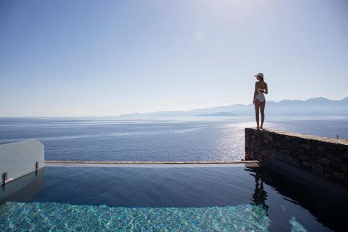 a person standing on a wall looking out over the water at Aquila Elounda Village Resort, Suites & Spa in Elounda