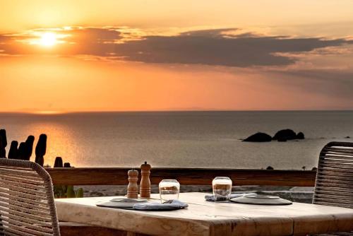 stół z dwoma kieliszkami wina i ocean o zachodzie słońca w obiekcie Mythic Paros , Adults Only w mieście Agia Irini Paros