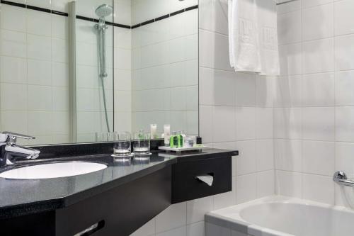 een badkamer met een wastafel, een spiegel en een bad bij NH Atlanta Rotterdam Hotel in Rotterdam