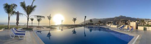 una piscina con sillas, palmeras y el océano en Turquaze Guesthouse, en Mascate