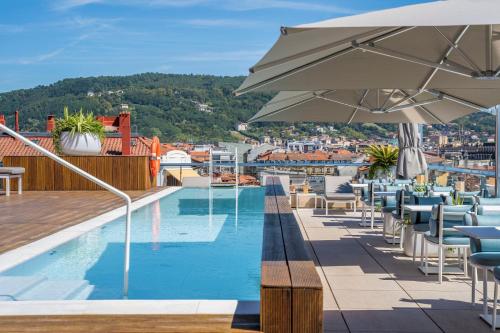 a pool on the roof of a building with chairs and an umbrella at Lasala Plaza Hotel in San Sebastián