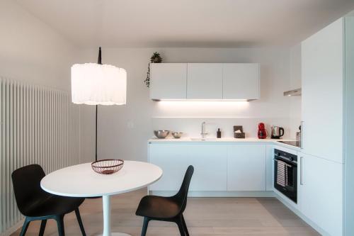 a white kitchen with a white table and chairs at La Palma 1 by Quokka 360 - modern panoramic lake view flat in Montagnola