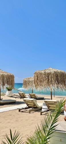 a group of chairs and umbrellas on a beach at Byblos Mare-The Exclusive Beach Front Villa in Skala Sotiros