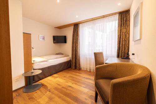 a bedroom with a bed and a chair and a window at Hotel Hohe Promenade in Arosa