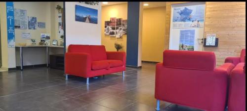 une salle d'attente avec des chaises rouges et des affiches sur le mur dans l'établissement Le Nivelet Les balcons d'Aix, à La Féclaz