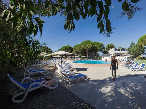 巴拉呂克萊班的住宿－Belambra Clubs Balaruc-les-Bains - Les Rives De Thau，一个人在带躺椅的游泳池边散步