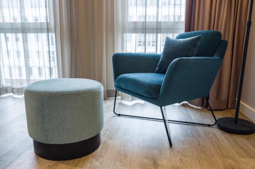 a blue chair and a stool in a room with windows at ibis Styles Bielefeld City in Bielefeld