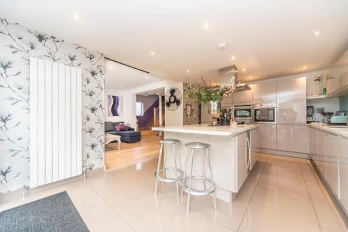 una cocina con armarios blancos y taburetes de bar en 6 bedrooms beautiful home 3 bathrooms, quiet location with garden near Legoland Windsor Heathrow, en Maidenhead