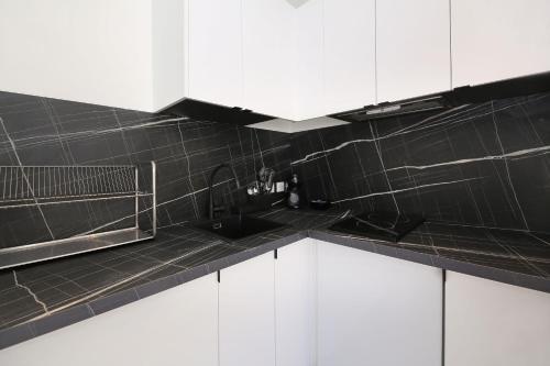 a black tiled kitchen with white cabinets and a sink at ZZZ poteau de Paris 4P in Paris