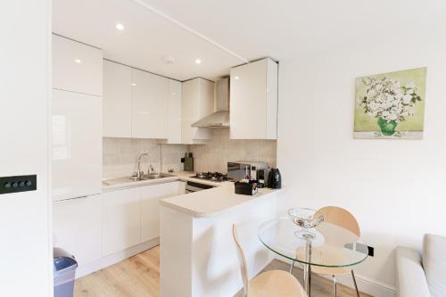 Penywern Apartment Earls Court في لندن: مطبخ مع دواليب بيضاء وطاولة زجاجية