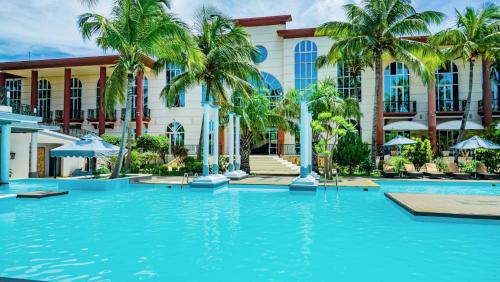 a swimming pool in front of a building with palm trees at Le Grand Hôtel Diego in Antsiranana