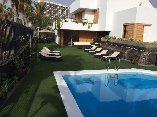 a backyard with a swimming pool and chairs and a building at Villa Las Americas in Playa de las Americas