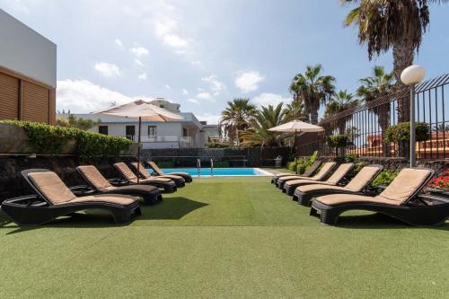 a row of lounge chairs next to a swimming pool at Villa Las Americas in Playa de las Americas