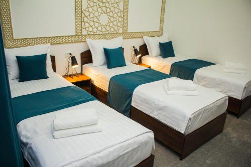 um quarto com três camas com lençóis azuis e brancos em Jahangir Boutique Bukhara em Bukhara