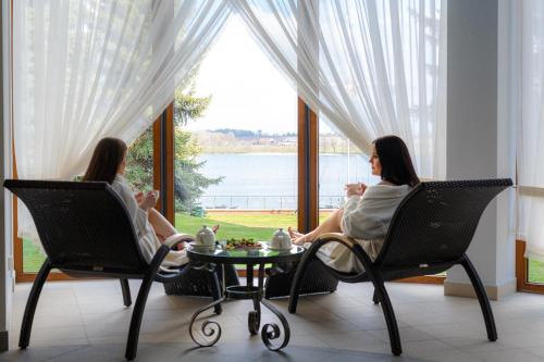 dwie kobiety siedzące w fotelach przed oknem w obiekcie Hotel Robert's Port w mieście Mikołajki