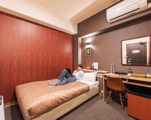 HOTEL RELIEF Kokura Station في كيتاكيوشو: امرأة جالسة على سرير في غرفة فندق