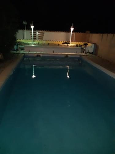 una piscina por la noche con dos luces. en Le CLOS D'AMANDINE, en Sallèles-dʼAude