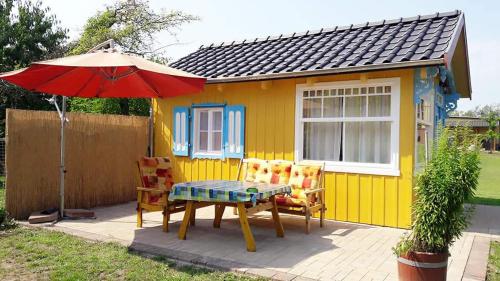 a yellow house with a table and chairs and an umbrella at Ferienbungalows am See in Altfriesack