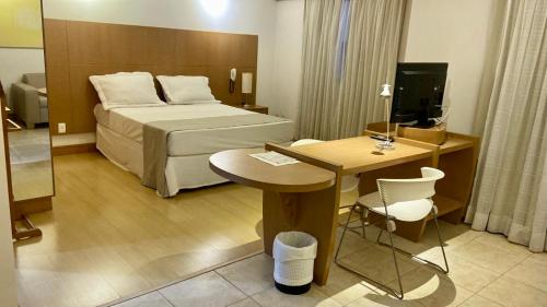 a hotel room with a bed and a table and a desk at Araucária Flat in Ribeirão Preto