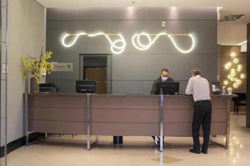 two people standing at a reception counter in an office at Araucária Flat Apto 305 in Ribeirão Preto