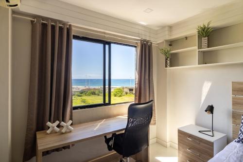 a bedroom with a desk and a window with the ocean at Cobertura Armação in Salvador
