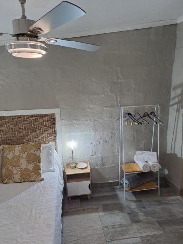 The Mustard Seed Guesthouse في بلومفونتين: غرفة نوم بسرير وطاولة ومروحة سقف