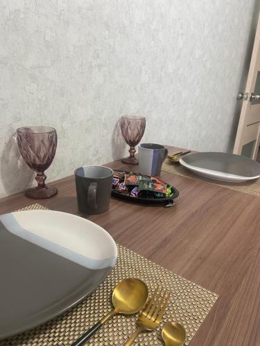 una mesa de madera con platos, vasos y cucharas en Комфортабельные - уютные апартаменты в Костанай мкр Береке1, en Kostanái