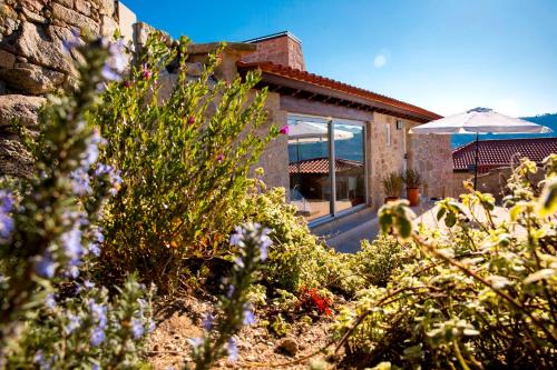 a house with a garden with flowers and an umbrella at Altiva - Casas de Selim in Arcos de Valdevez