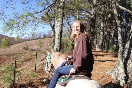 a girl sitting on a horse in the woods at Arrowmont Stables & Cabins in Cullowhee