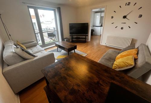 a living room with a couch and a clock on the wall at River View Apartment - Central Dundee - Free Private Parking - Sky & TNT Sports - Lift Access - Superfast WIFI - Quiet Neighbourhood - 2 Bathrooms - Amazing Views - Balcony & Courtyard - Long Stays Welcome in Dundee