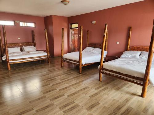 three beds in a room with a wooden floor at Ishasha Pride Lodge in Kihihi
