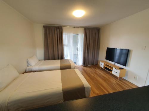 Habitación de hotel con 2 camas y TV de pantalla plana. en Ocean Inn Motel, en Auckland