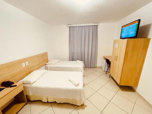 a hotel room with two beds and a television at Pioneiro Hotel in Teixeira de Freitas