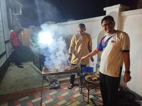 two men are cooking food on a grill at BERUNTUNG KE BARI RESORT @ PANTAI PENARIK in Kampong Bari Kechil