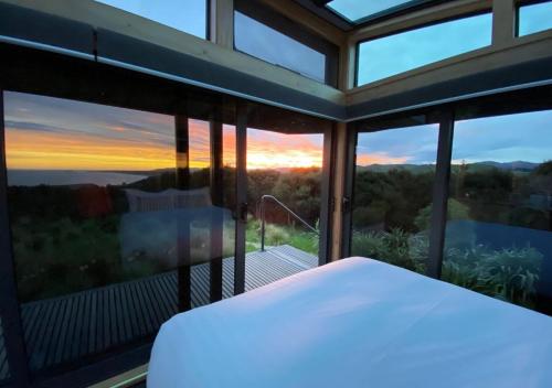 a bedroom with a view of the sunset through windows at Korimako PurePod in Scargill