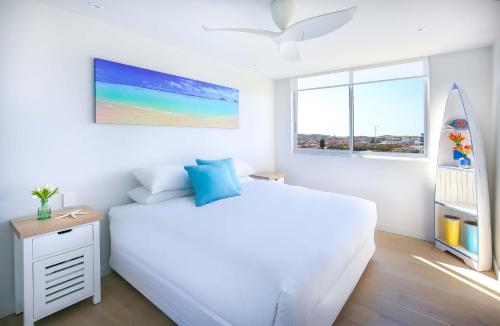 Habitación blanca con cama y tabla de surf en Bondi Aqua Vista - Walk to beach and shops, en Sídney