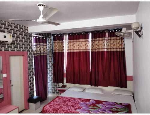 a bedroom with a bed with red curtains and a ceiling fan at Hotel Agrawal, Pachmarhi in Pachmarhī