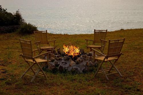 three chairs sitting around a fire in a field at Aroura Homes 4BR Beachfront Villa in Spetses