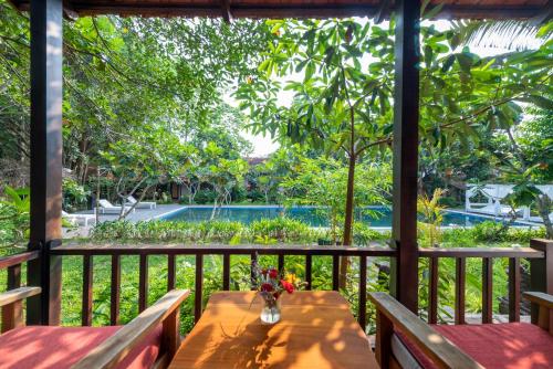 un porche de madera con bancos y una mesa con flores en An Nhien Retreat, en Phu Quoc