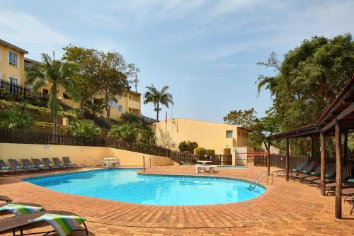 a large swimming pool in a courtyard with trees and buildings at First Group Chaka's Rock Chalets in Ballito
