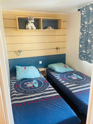 two beds in a small room with a teddy bear on a shelf at Mobil home 8 personnes camping L'Elysée Vagues Océanes in Le Grau-du-Roi