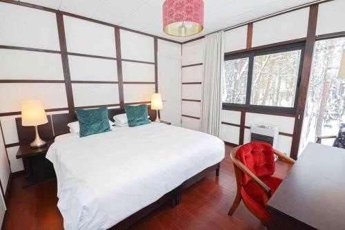 a bedroom with a white bed and a chair and windows at Hakuba Cottage Momiji in Hakuba