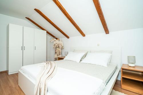 a white bedroom with a white bed and wooden ceilings at Apartment Sunday in Mokošica