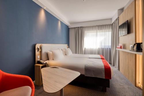 Holiday Inn Express Mechelen City Centre, an IHG Hotel في ميشيلين: غرفة بالفندق سرير وكرسي احمر